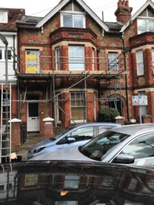Two-lift window access scaffold at first-floor level on a red brick house in Dene Road, Guildford